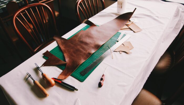 Table with large scrap of leather on top of a cutting board with many tools