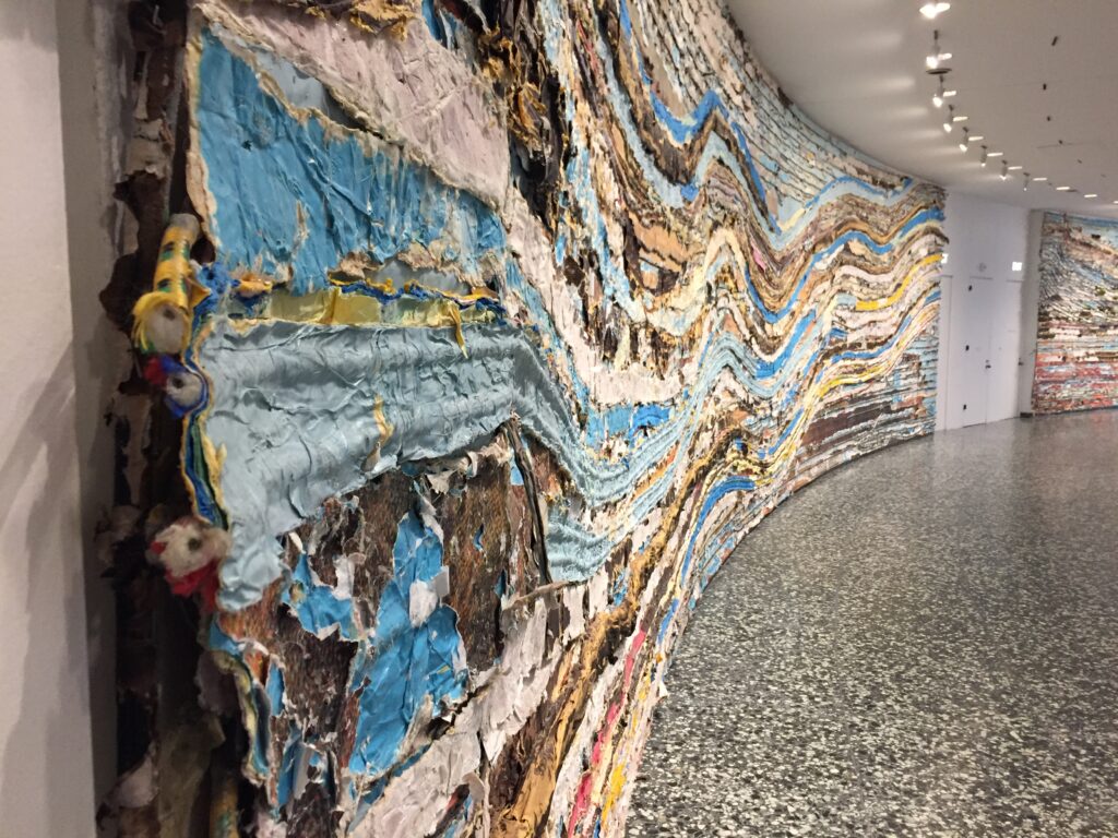 View of Mark Bradford's work Pickett's Charge at the Hirshhorn Sculpture Museum - photo shows many layers of papers and ropes along a curved wall to make a colorful mural