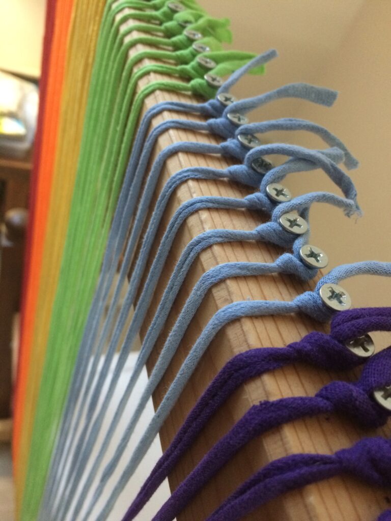 Rainbow warp on Trashmagination's tapestry loom - colorful strings attached to screws