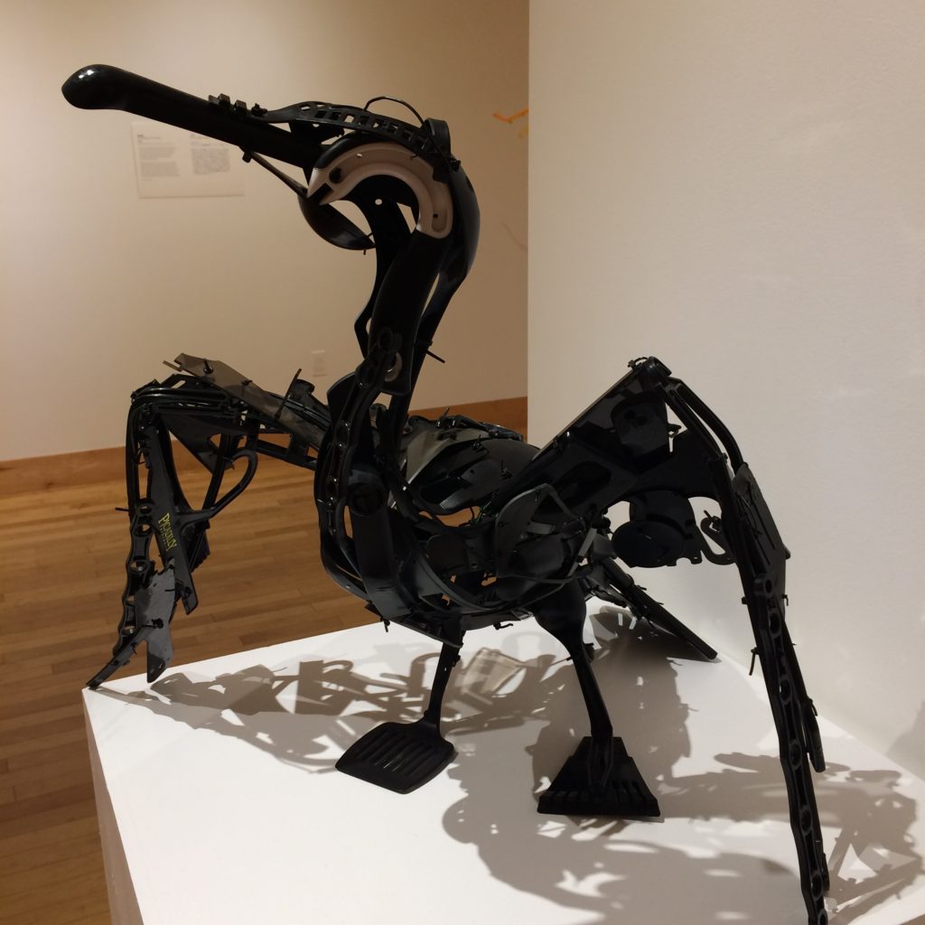 A black sculpture of a cormorant sea bird with its arms outstretched to warm in the sun - located in an art gallery