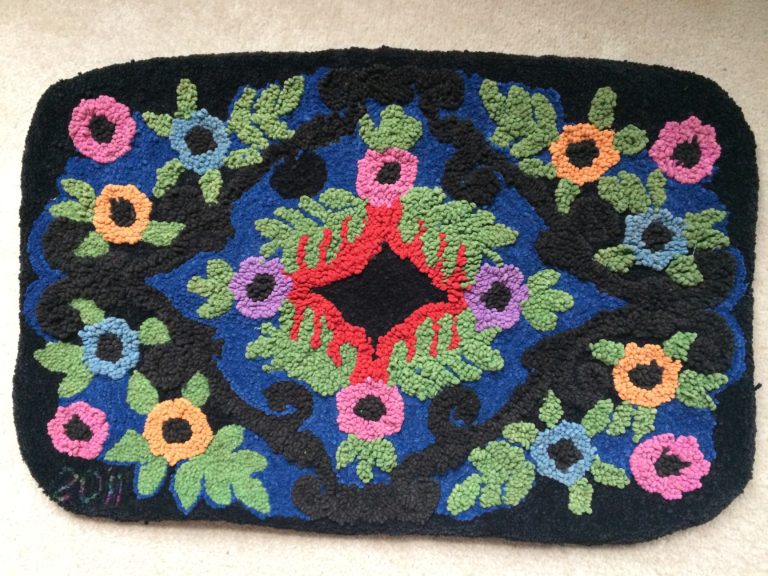 Rectangular hooked rug with pink, purple, blue and orange flowers in a traditional design
