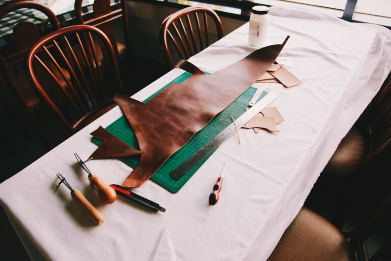 Table with large scrap of leather on top of a cutting board with many tools