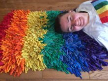 Woman laying on a very fluffy rug made from recycled tshirts in rainbow colors