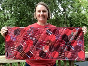 Woman holds up a wide rectangular red quilt with hexagon designs