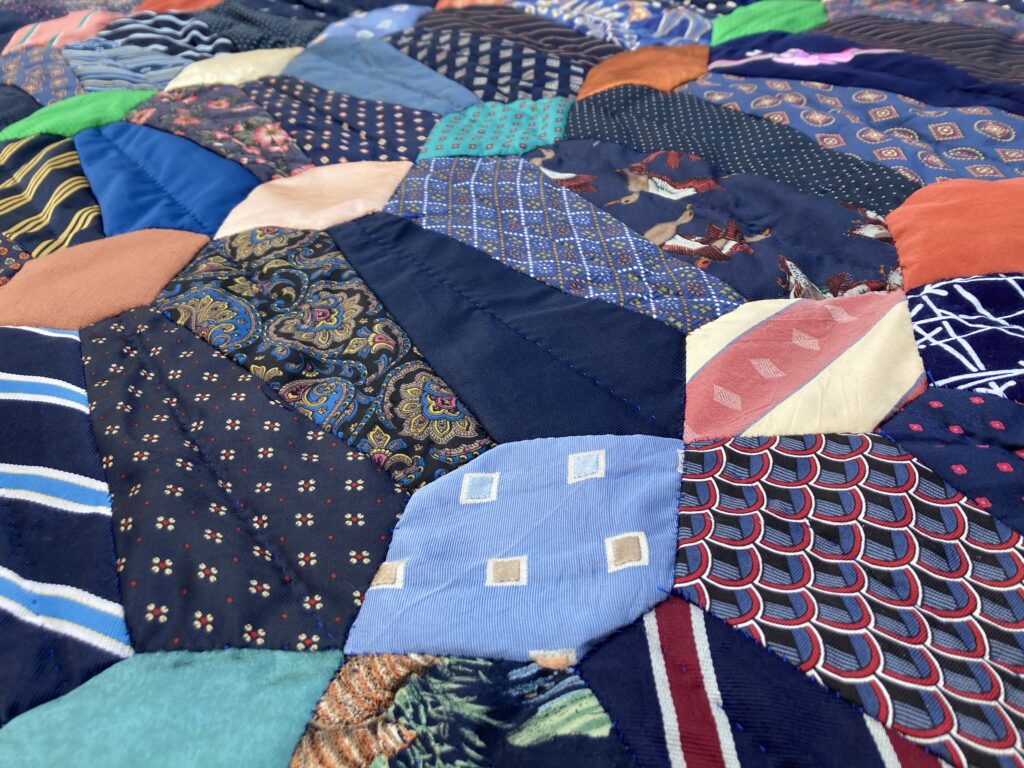 Close-up of a quilt made from upcycled neckties - mostly navy blue with some pops of color