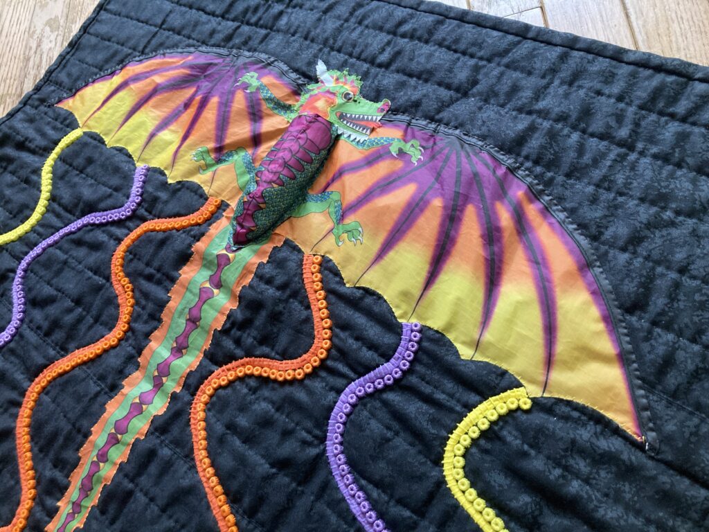 Quilt with black background and dragon flying upwards purple orange and yellow