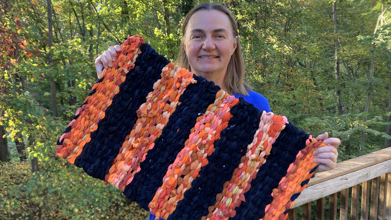 Woman holds up a rug that is woven from orange and black t-shirts